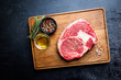 Raw fresh meat Ribeye Steak and seasonings on dark background, top view with copy space
