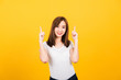Asian happy portrait beautiful cute young woman teen standing wear t-shirt makes gesture two fingers point upwards above looking to camera isolated, studio shot on yellow background with copy space