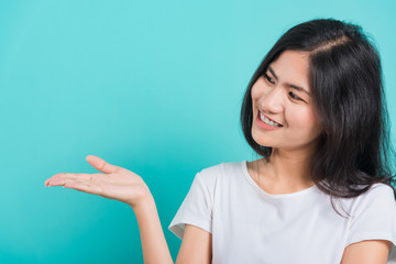 Wall Mural - Portrait Asian beautiful young woman standing wear t-shirt, She showing hand to presenting product and looking to product, shoot photo in a studio on blue background, There was copy space