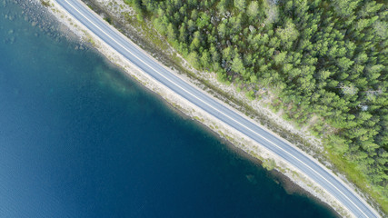 Wall Mural - Beautiful aerial view of road between green summer forest and blue lake in Finland. Scandinavia. Top down view.