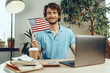 © fotofabrika - Young bearded businessman sitting at table with laptop and american flag