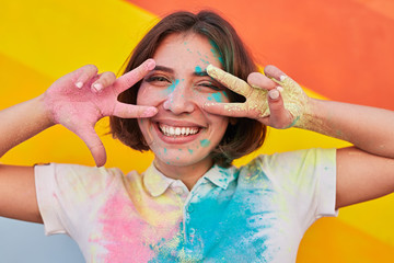 Wall Mural - Happy young woman gesturing V sign during paint festival