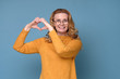 © Viktor Koldunov - Beautiful caucasian woman showing heart shape isolated on blue background. Positive facial human emotion.