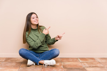 Young caucasian woman sitting on the floor isolated excited pointing with forefingers away.