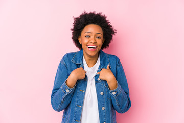 Wall Mural - Young african american woman against a pink backgroound isolated surprised pointing with finger, smiling broadly.