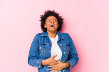 Wall Mural - Young african american woman against a pink backgroound isolated laughs happily and has fun keeping hands on stomach.