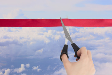 Wall Mural - The beginning of the tourist season. A hand cuts a red ribbon with scissors overlooking the fluffy clouds in the blue sky