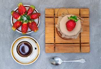 Strawberry berries on a white plate on a cutting Board on a gray background with a Cup of tea and a spoon. Flatly. The view from the top.