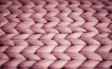 Background. Knitted Fabric Made Of Pink Merino Wool. Large Weave. Pattern Of Pigtails.