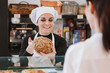 © Eva Blanco/Westend61 - Happy female baker selling wholegrain bun to customer at bakery