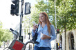 © PETE  MULLER/Westend61 - Happy young woman using smart phone while standing by hire bike in city