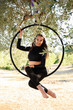 Acrobat, young girl making a pose on an aerial hoop among olive trees in summer. Acrobat training during summer, outdoors.