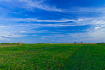 Wall Mural - picturesque horizon landscape scenic view of agriculture rural field with stack of hay on green grass end of summer season in August month, clear weather evening