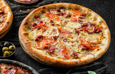 Canvas Print - Pizza Pepperoni with prosciutto, sausage, cheese parmesan, tomatoes and onion rings on stone black background. Fast food lunch for picnic company, top view, selective focus