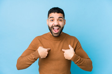 Wall Mural - Young latin man against a blue  background isolated surprised pointing with finger, smiling broadly.