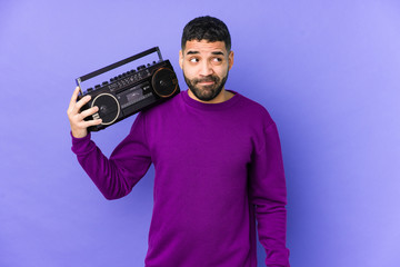 Wall Mural - Young arabian man holding a radio cassette isolated Young arabian man listening music confused, feels doubtful and unsure.