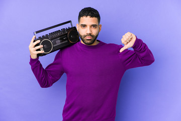 Wall Mural - Young arabian man holding a radio cassette isolated Young arabian man listening music showing a dislike gesture, thumbs down. Disagreement concept.