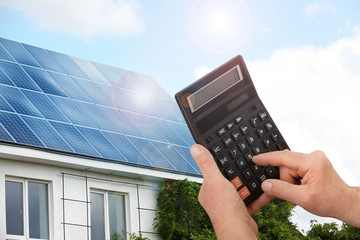 Wall Mural - Man using calculator against house with installed solar panels. Renewable energy and money saving