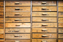 Archive Representing Identical Light Brown Wooden Drawers With Rectangular Handles And Numbers On Uneven Surface With Spots And Words In Workshop