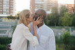 © Jake Jakab/ADDICTIVE STOCK - Positive romantic multiethnic couple in white shirts kissing and bonding while standing on street against modern residential buildings on sunny summer day