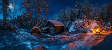 Small Wooden House Located In Picturesque Winter Forest Covered By Snow Near Bonfire At Night