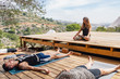 © Javier De La Torre/ADDICTIVE STOCK - Female yoga trainer sitting in Lotus pose instructing students relaxing in Corpse asana after finishing outdoor workout on sunny day
