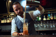 © Luis Gomez/ADDICTIVE STOCK - Professional young bartender pouring cocktail from shaker into a glass full of ice in a bar