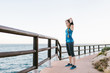 © Lightsy/ADDICTIVE STOCK - Side view of fit female in activewear standing on promenade and stretching arms during training near sea