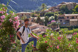 © Philippe Degroote/ADDICTIVE STOCK - Side view of hipster male tourist in stylish outfit with backpack standing near fence with blooming bushes and enjoying picturesque scenery of old town located among green hills in summer day