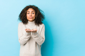 Wall Mural - Young african american curly hair woman folding lips and holding palms to send air kiss.