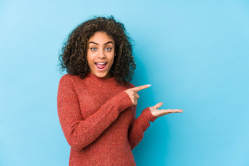 Wall Mural - Young african american curly hair woman excited holding a copy space on palm.