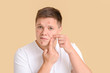 © Pixel-Shot - Teenage boy with acne squishing pimples on color background