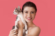 © Strelciuc - Freckled caucasian woman with naked shoulders posing on a pink wall with a cat smiling at camera