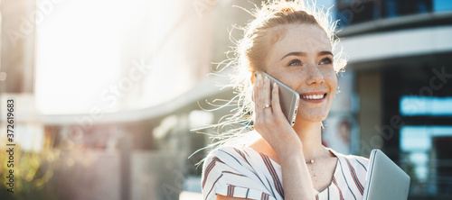 Fotografía Red haired businesswoman with freckles discussing on phone and posing with a lap