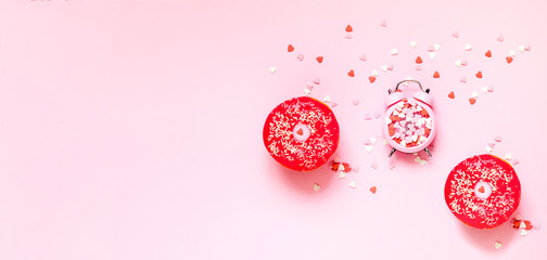 Wall Mural - Colored donut with colorful sprinkles and pink alarm clock with decorative colored hearts on pink background. Donut day concept.