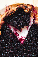 Canvas Print - A close-up of a black currant galette on baking paper on white background, a slice with a piece bitten off, top view