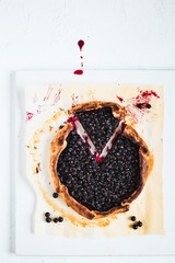 Wall Mural - A black currant galette on baking paper on white background, top view