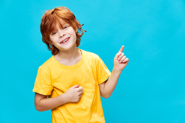 Sticker - child with red hair on a blue background points up and laughs Copy Space