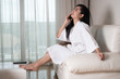 © Thicha - Young attractive Asian woman in a bathrobe sitting on the sofa who  talking on the phone at the room