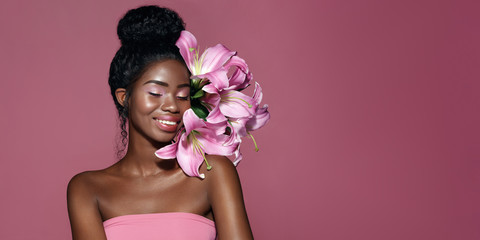 Wall Mural - fashion portrait of young african american model with pink art make up posing with lily flowers agai