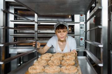 Wall Mural - Close up of young caucasian woman baker is holding a tray with fresh bagels and looking to them at baking manufacture factory.