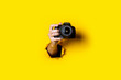 Leinwandbild Motiv Man's hand holding a camera on a bright yellow background.