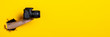 © Alex - Female hand holding a camera on a bright yellow background. Banner.