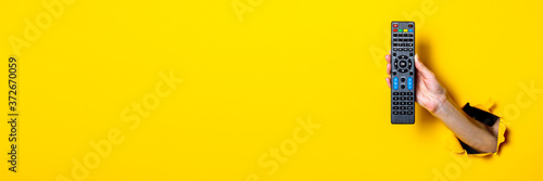 Cuadros en Lienzo Female hand holding a TV remote control on a bright yellow background
