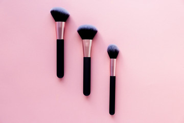 Three makeup brushes of different sizes lie on a pink background. Applying cosmetics to the face, personal care. Place for text.