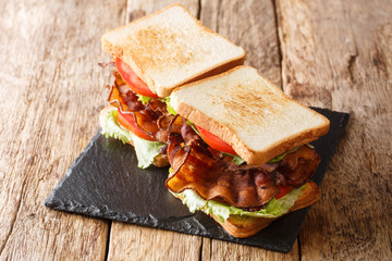 Two blt sandwiches with bacon, fresh salad and tomatoes are served on a slate board on the table. horizontal