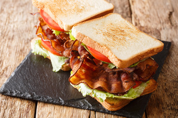 Wall Mural - American fast food blt sandwich with bacon, fresh salad and tomatoes close-up on a slate board on the table. horizontal