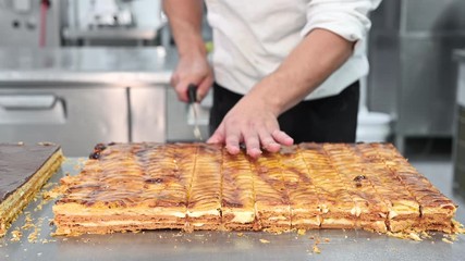 Wall Mural - Close-up of a pastry chef cutting a large cake in portions at pastry shop. High quality 4k footage