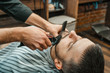 © Natalya Lys - Beauty shop for men. Shaving a beard in a barbershop. Barber cuts his beard with a razor and clipper. close up Brutal haircuts. Hairdresser equipment. Selective focus.