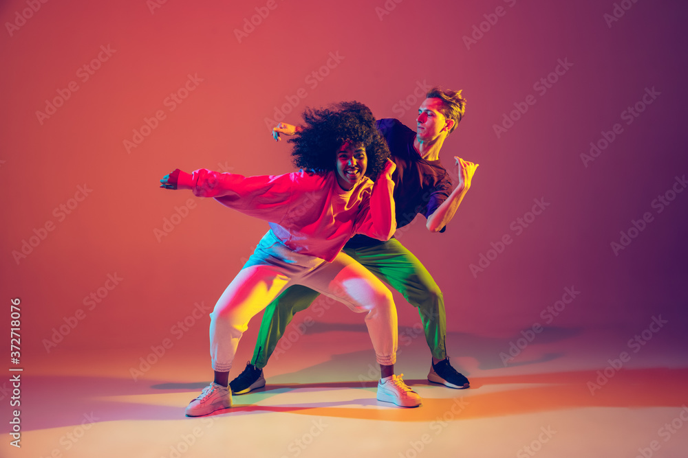 Drive in motion. Stylish man and woman dancing hip-hop in bright clothes on green background at dance hall in neon light. Youth culture, movement, style and fashion, action. Fashionable portrait. - obrazy, fototapety, plakaty 